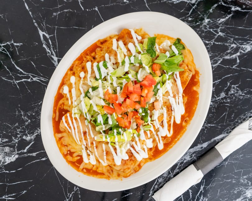 A plate of enchiladas topped with red sauce, melted cheese, lettuce, diced tomatoes, and sour cream.