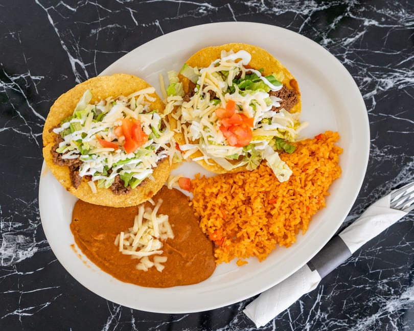 Two crispy tacos with ground beef, lettuce, cheese, and tomatoes, served with rice and refried beans.