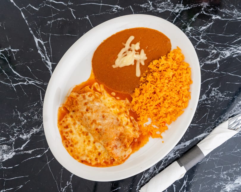 A plate of enchiladas covered in melted cheese, with a side of rice and refried beans.