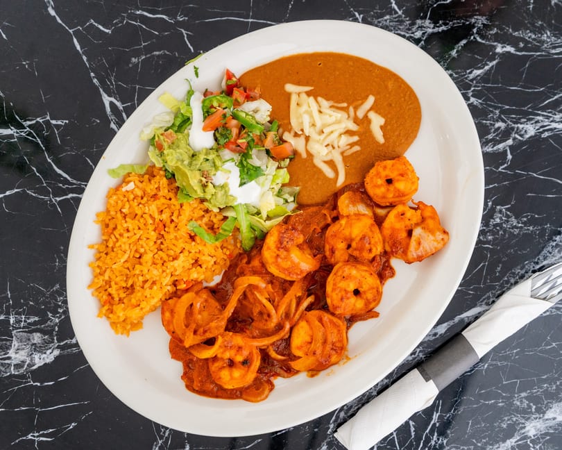 A white plate with shrimp in red sauce, rice, refried beans, and a side salad.