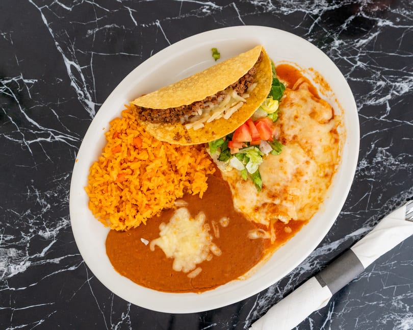 A Mexican combination plate with a taco, rice, refried beans, and two cheese enchiladas.