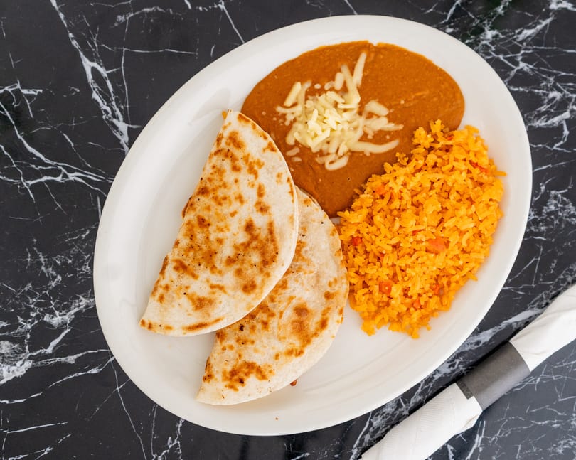 A white oval plate with two quesadillas, refried beans with cheese, and orange rice.